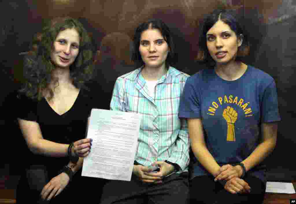 2012年8月17日俄罗斯女庞克摇滚乐队“Pussy Riot”的三名歌手奥尔约其纳(图左),萨姆泽维奇(图中),和托洛尼克娃(图右)坐在俄罗斯一个法庭拘禁她们的玻璃隔离的角落,奥尔约其纳展示法院的判决书