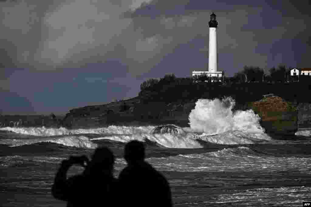People watch waves in front of a lighthouse near the central beach, in Biarritz, southwestern France.