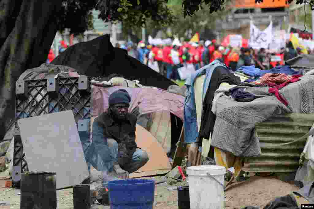 A homeless man prepares food as marchers pass by after the members of various labor unions embarked on a nationwide strike over the high cost of living in Cape Town, South Africa.