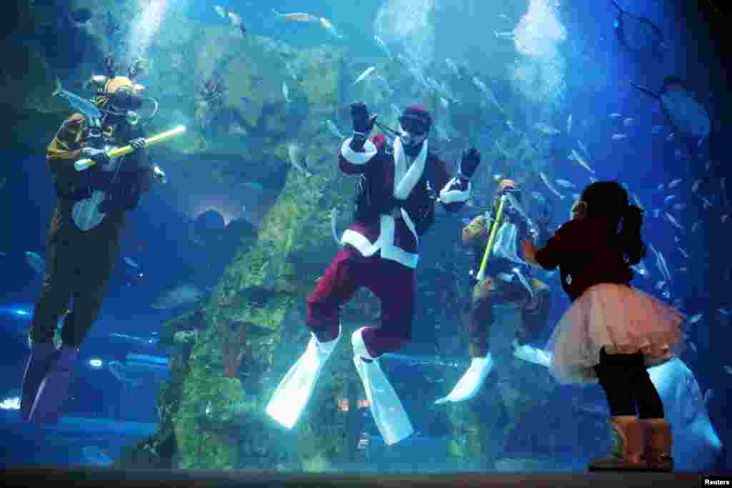 A girl looks at divers in Santa Clause and Rudolph the Red Nosed Reindeer costumes during a promotional event for Christmas at an aquarium in Seoul, South Korea.
