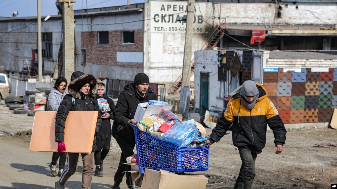 FILE - Local residents carry water from the food warehouse, on the territory which is under the Government of the Donetsk People's Republic control, on the outskirts of Mariupol, Ukraine, March 18, 2022. 