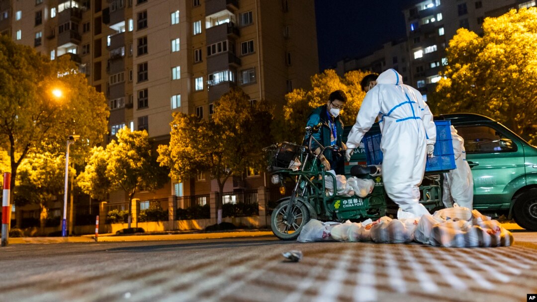 Deliverymen wearing protective suits carry bags of food at the gate of a residential community in Shanghai, April 11, 2022. 