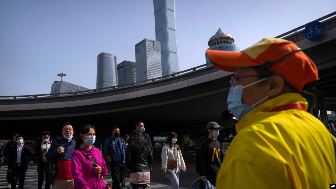 Commuters wearing face masks walk across an intersection in the central business district in Beijing, April 12, 2022.