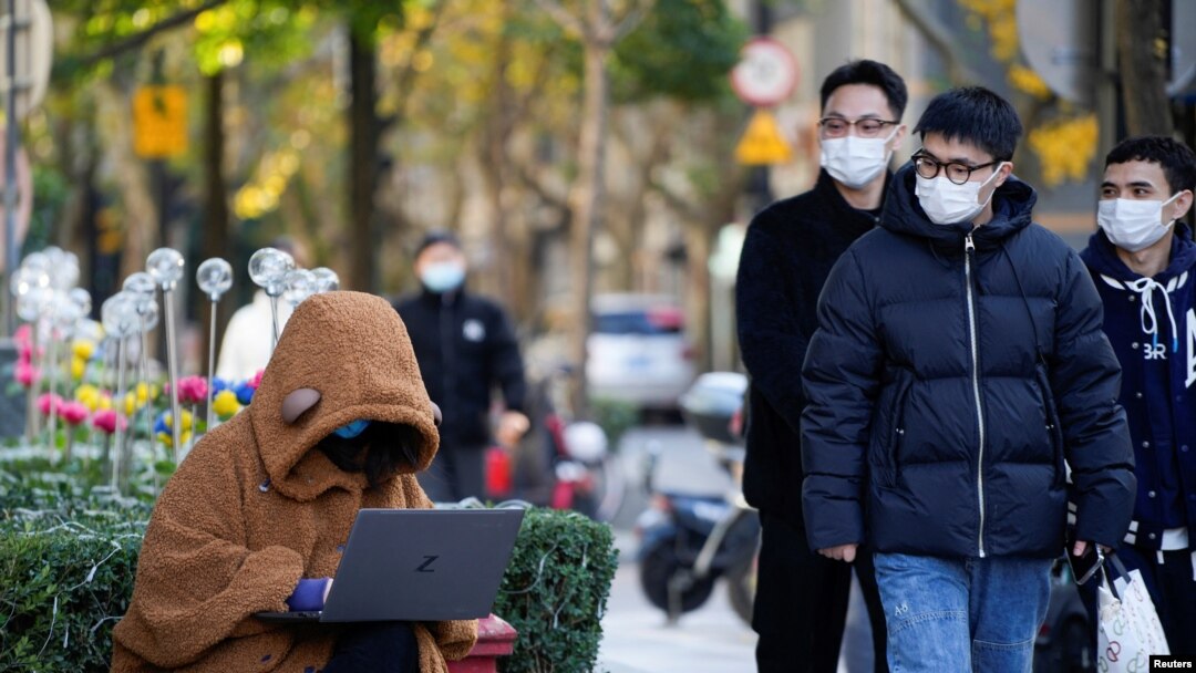 A woman wearing a face mask looks at her laptop on a street, as coronavirus disease (COVID-19) outbreaks continue in Shanghai, China, Dec. 14, 2022.