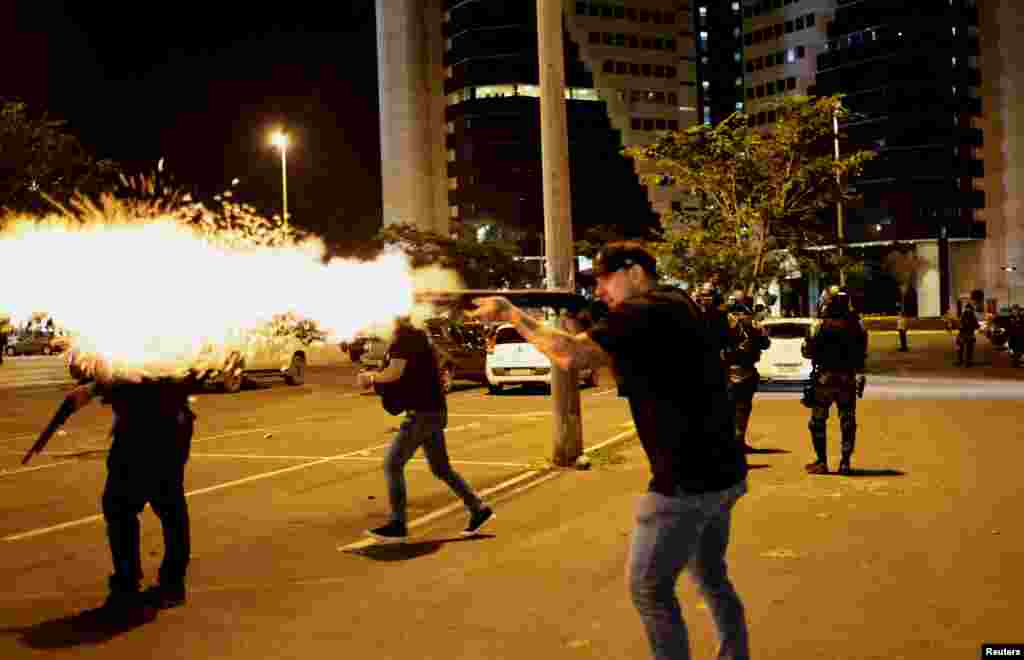 A police officer fires a shotgun as supporters of Brazil's President Jair Bolsonaro protest after supreme court justice Alexandre de Moraes ordered a temporary arrest warrant of indigenous leader Jose Acacio Serere Xavante for alleged anti-democratic acts, in Brasilia, Dec. 12, 2022.