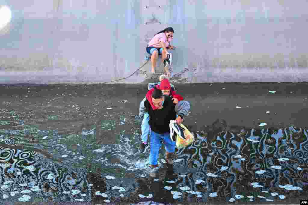 A family of migrants from Columbia makes their way through a water canal in the U.S.-Mexico border wall in El Paso, Texas, Dec. 19, 2022.