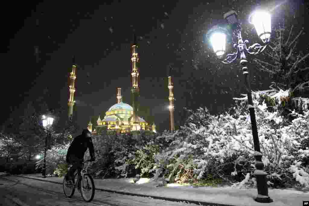 A man rides a bicycle during a snowfall, as the main Mosque is illuminated for New Year celebrations in downtown Grozny, the capital of Chechnya, Russia.