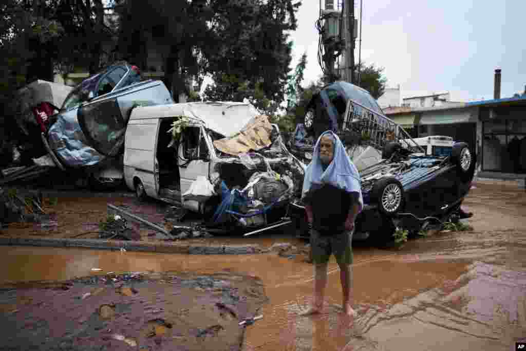 A barefoot man stands in front of a pile of vehicles in the municipality of Madra western Athens, Greece. Flash floods in the Greek capital's western outskirts turned roads into raging torrents of mud and debris, killing at least nine people, inundating homes and businesses and knocking out a section of a highway.