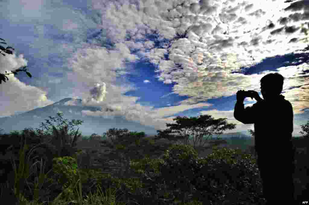 A man takes a photo as a puff of smoke comes from Mount Agung volcano, taken from the Rendang sub-district in Karangasem Regency on Indonesia's resort island of Bali.