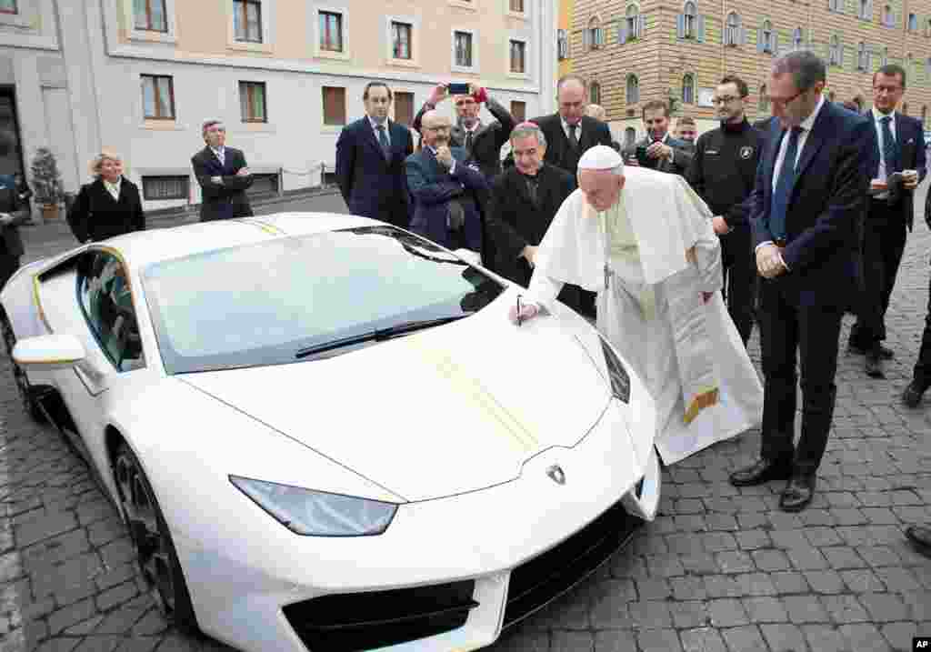 Pope Francis writes on the bonnet of a Lamborghini donated to him by the luxury sports car maker, at the Vatican. The car will be auctioned off by Sotheby's, with the proceeds going to charities including one aimed at helping rebuild Christian communities in Iraq that were devastated by the Islamic State group.