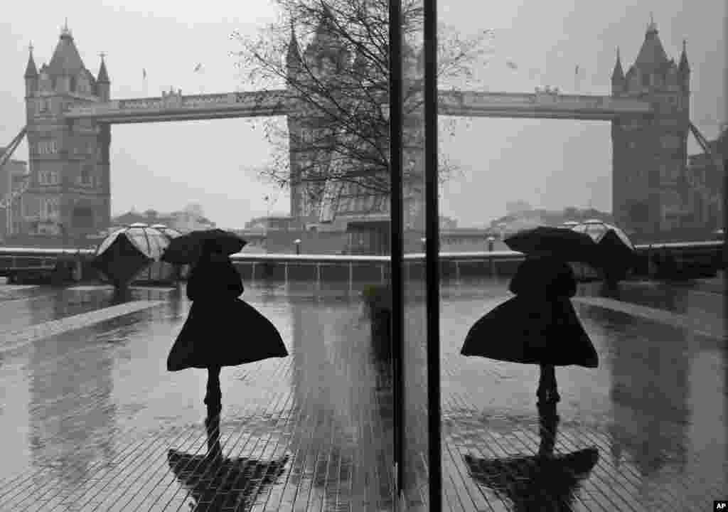 A woman is reflected in a window as she braves wind and rain while walking towards Tower Bridge in London during England's third national lockdown to curb the spread of coronavirus.