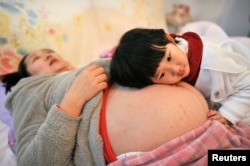 一名女孩趴在怀孕的妈妈的肚子上