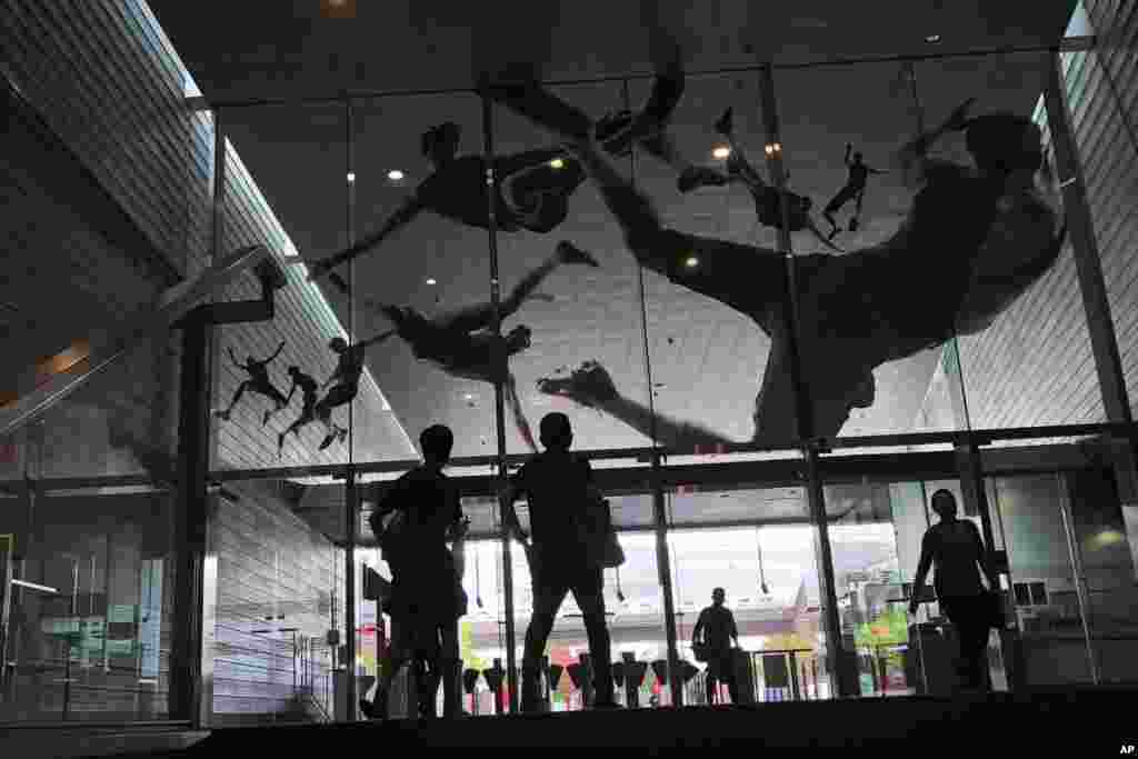People look at the glass entrance of a subway station in Singapore which is decorated with decals of athletes in action.