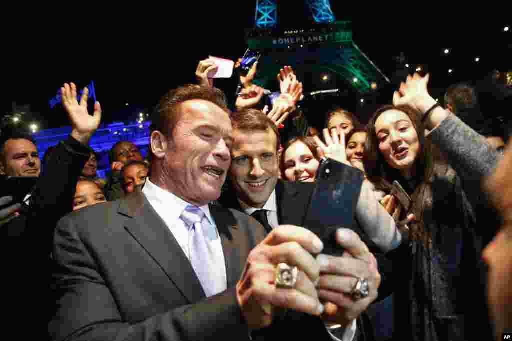 France's President Emmanuel Macron, center, and former California Governor Arnold Schwarzenegger take a selfie with young people aboard a boat cruising on the Seine river in Paris, Dec. 12, 2017.
