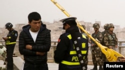 在中国新疆维吾尔自治区喀什的一条街上，警察检查一名男子的身份证，旁边有安全人员（2017年3月24日）