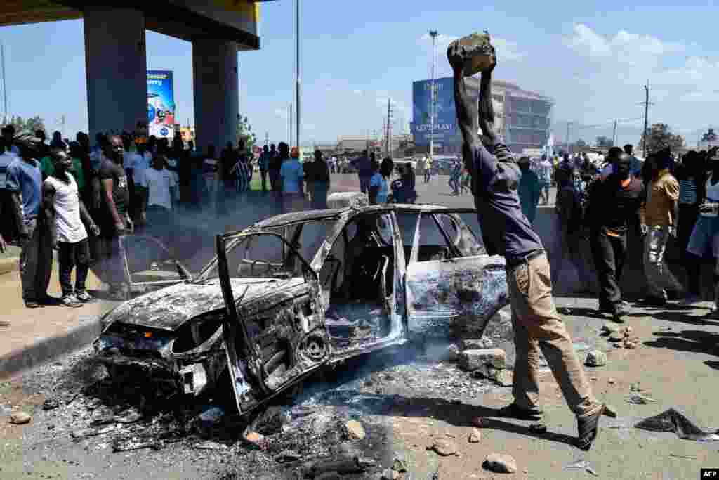 A man throws a stone on a burnt car as supporters of Kenya's opposition party National Super Alliance (NASA) demonstrate in Kisumu.
