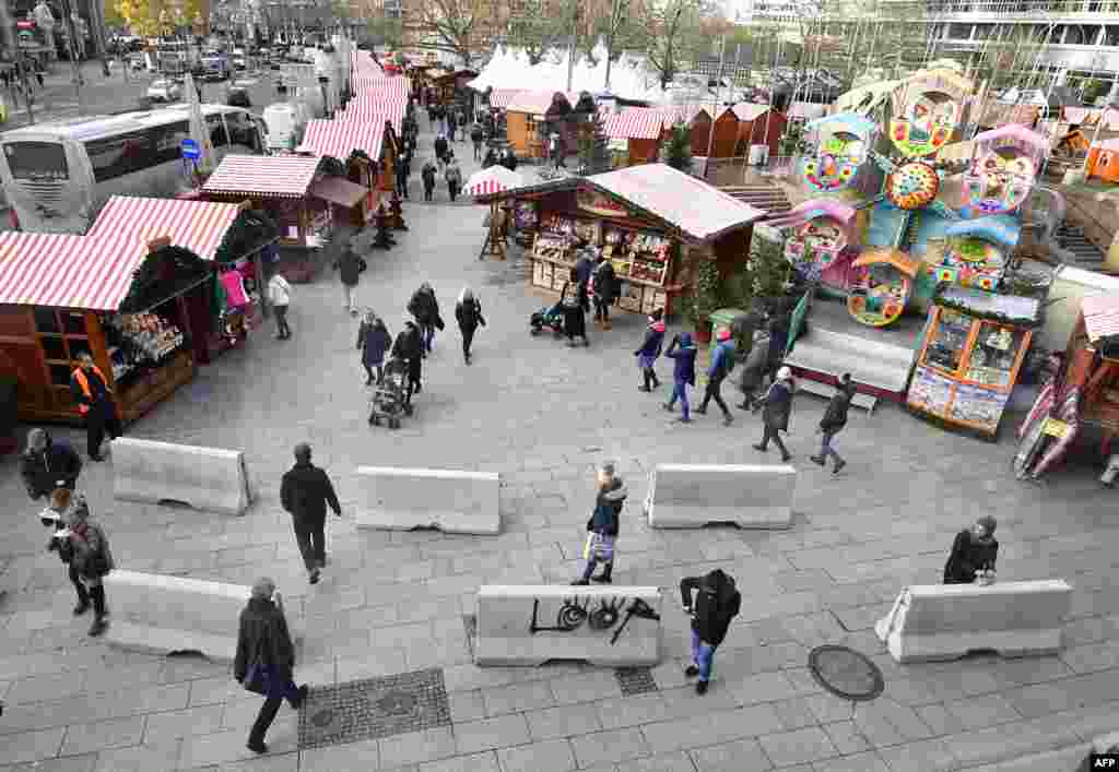 People walk past concrete barriers erected for the security of the Christmas market at Berlin's Breitscheidplatz square as the market opens to the public, Germany.