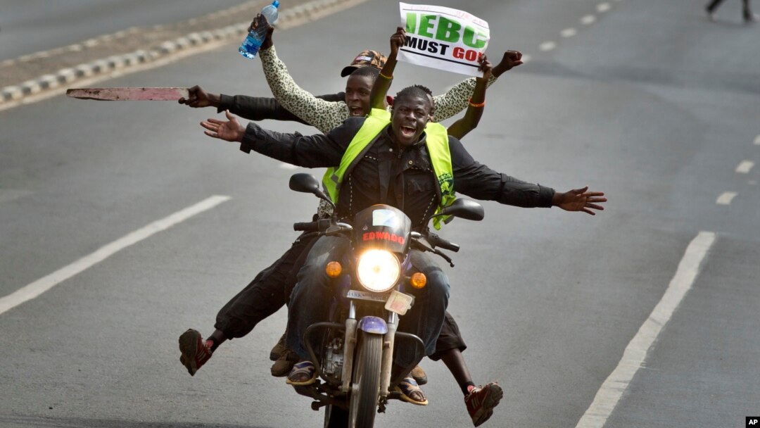 FILE - A motorcycle carrying protesters holding a placard using the acronym of the national electoral commission, drives ahead of demonstrators on foot calling for the disbandment of the commission over allegations of bias and corruption, in Nairobi, Kenya, June 6, 2016.