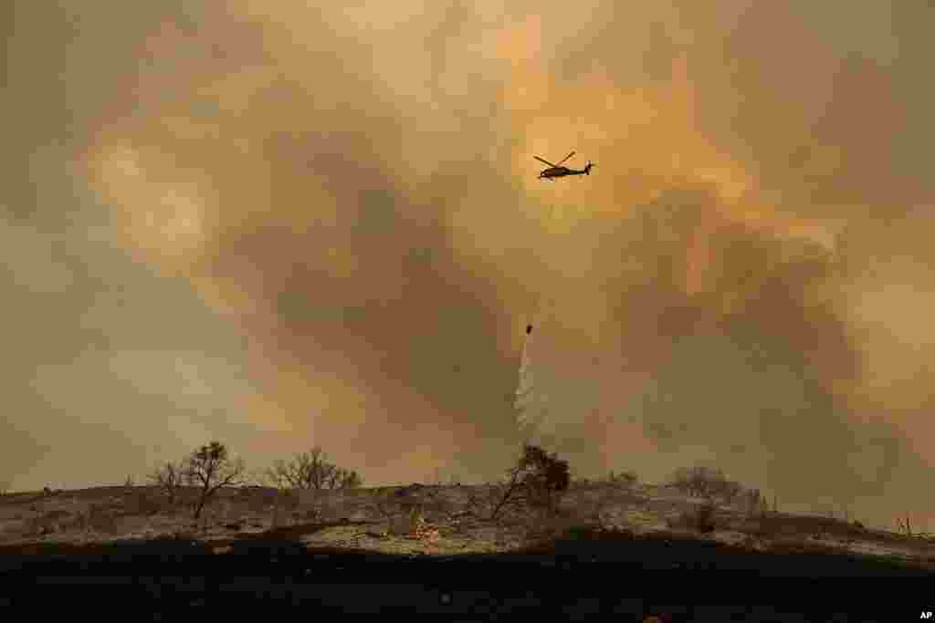 A helicopter drops water while trying to keep a wildfire from jumping Santa Ana Road near Ventura, California, Dec. 9, 2017.