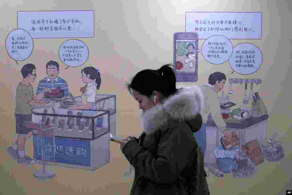 2019年1月3日在北京一个地铁站,女子看着手机,走过推广iPhone的壁画。